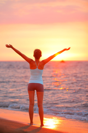 Happy freedom woman relaxing arms up at beach sunset during fitness yoga. Summer vacation person carefree on holidays travel.